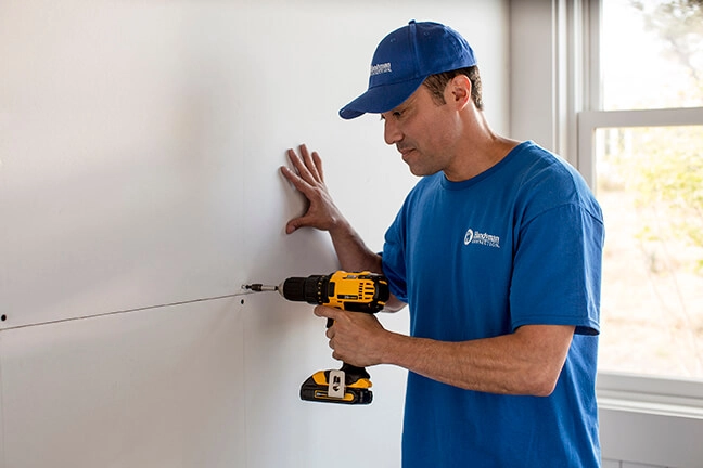 A photo of a Handyman Connection worker installs drywall inside a home