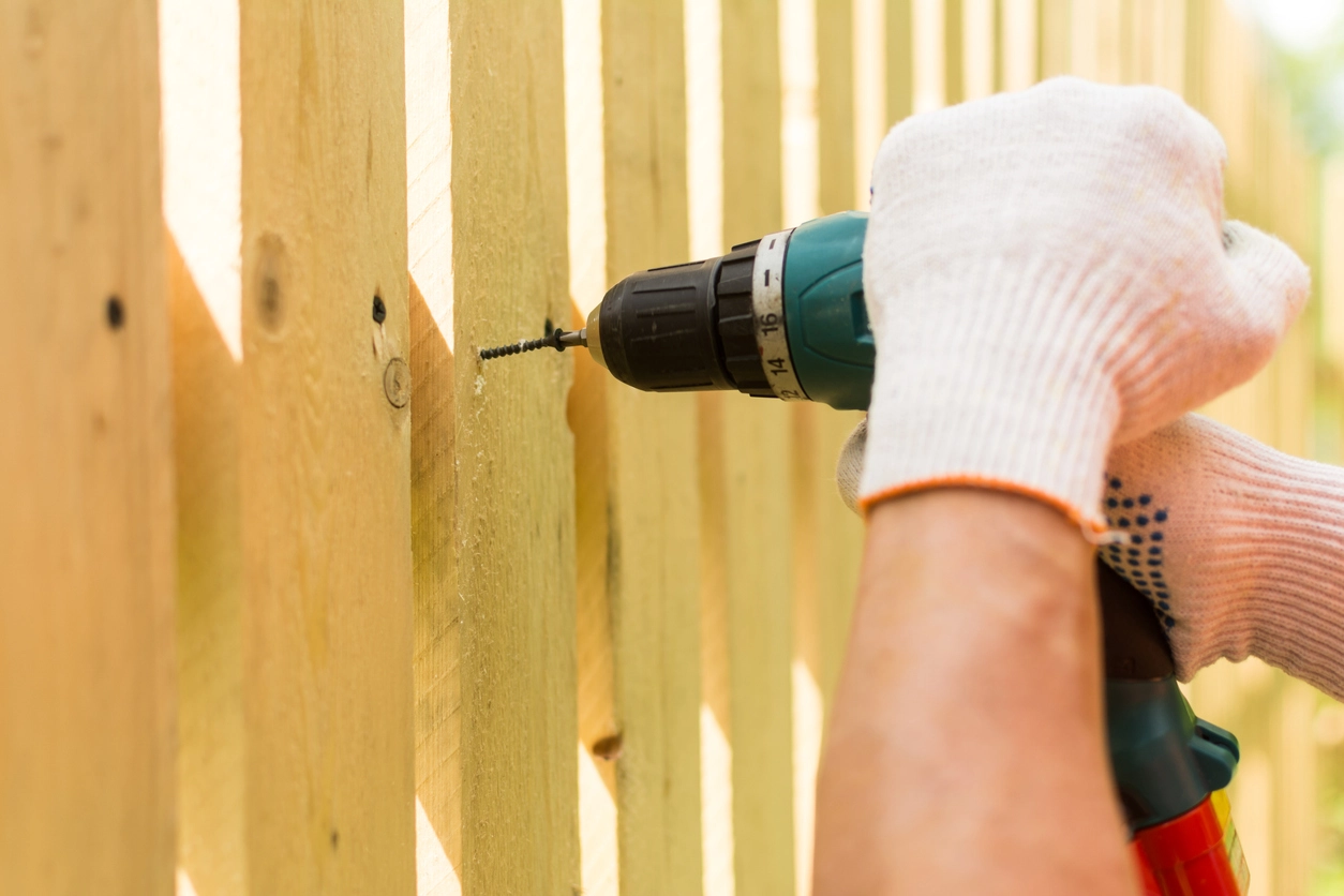 A photo of a screw being driven into the boards of a fence