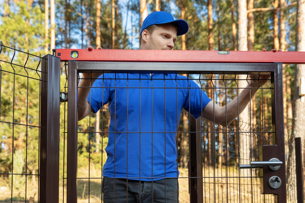 A photo of a HMC worker installing a fence gate and making sure it is level.