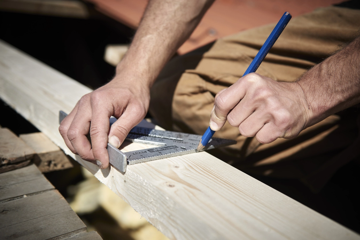 carpentry worker uses speed square to mesaure a 2x4